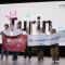 People cheering on a scenario in front of a big screen that says "Turin"
